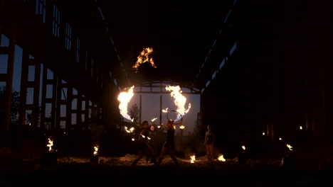 Four-women-in-leather-clothes-with-fire-dance-and-show-fire-show-a-man-with-a-flamethrower-in-the-back-plays-with-the-flame-in-slow-motion